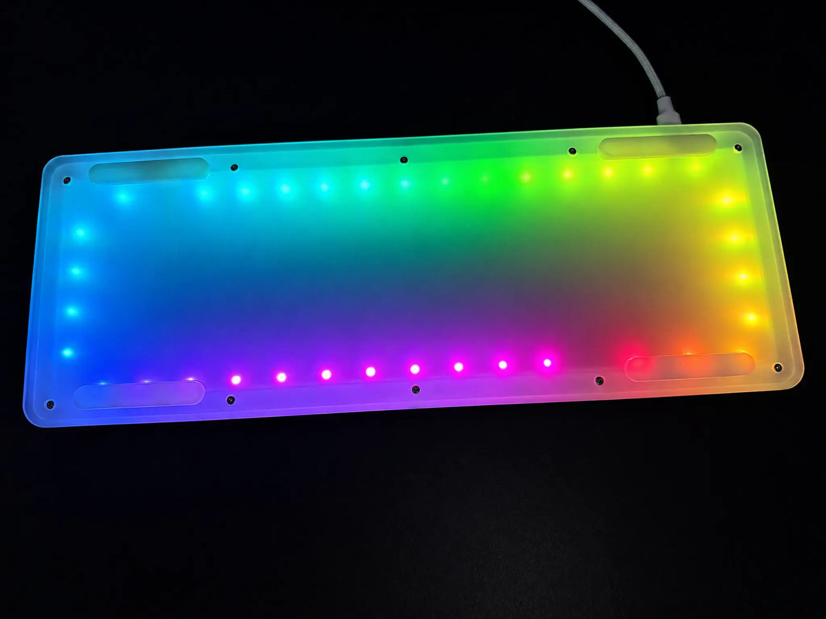 Odin Gaming Aurora65 LITE keyboard underside showing multicolor RGB underglow through the translucent bottom case and a connected USB cable.
